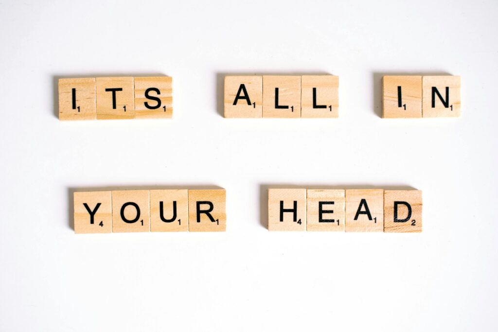 Wooden Scrabble tiles arranged to spell 'ITS ALL IN YOUR HEAD' on a white background.